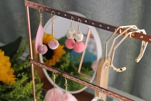 Detail of rose gold jewelry stand with pink feather earrings and a pine wood base