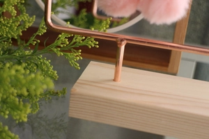 Detail view of rose gold earring rack with pine wood base and soft pink pompom decor