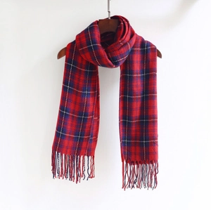 Detailed view of red and blue plaid winter scarf with fringe tassels on a wooden hanger