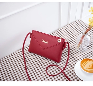 Detail of red leather crossbody bag with gold Chleo logo and leaf zipper pull