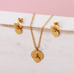 Golden heart jewelry set with Roman numerals and Love engraving on a pink background