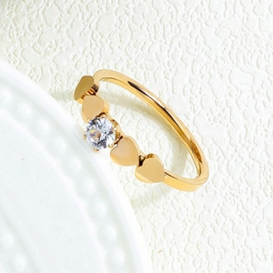 Golden stainless steel heart ring with central round zircon on a textured white surface