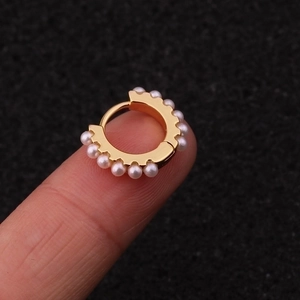 Elegant gold hoop earrings with white pearl inlay displayed on a fingertip for scale