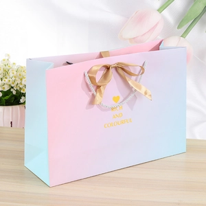 Pink and blue gradient gift bag with gold ribbon bow on a wooden surface