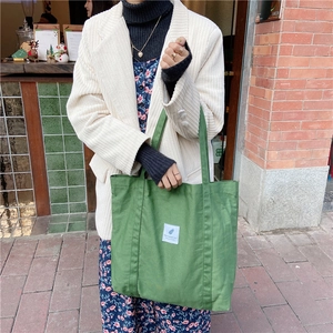 Casual green canvas tote bag with a white woven label, styled over a beige corduroy jacket