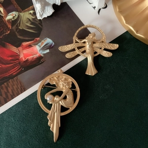 Close-up of matte gold Art Nouveau brooches with fairy relief and a single pearl inlay