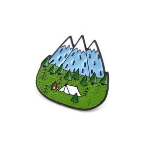 Detail view of enamel camping brooch with blue mountains, green trees, and white tent