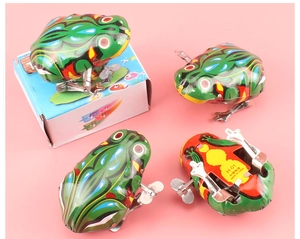 Detailed view of four classic green tin frogs with vintage packaging on pink background