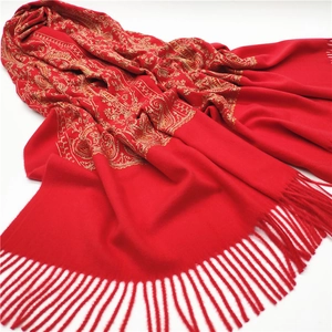 Detailed close-up of golden paisley embroidery and red tassels on a cashmere shawl