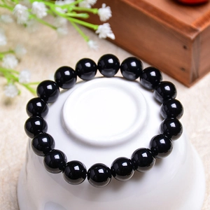 Polished natural black agate bead bracelet displayed on a white ceramic base with dry flowers