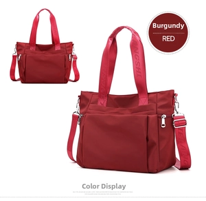 Detail view of wine red nylon tote bag featuring side zippers and adjustable logo strap