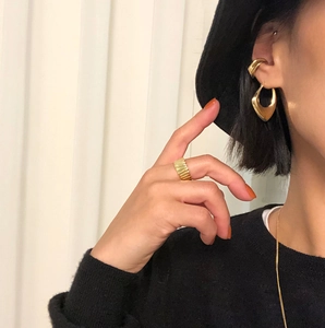 Close-up of elegant gold geometric heart earrings and textured ring on a model
