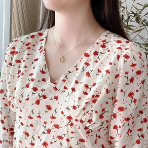 Detail shot of a minimalist gold geometric circular pendant necklace on a floral dress