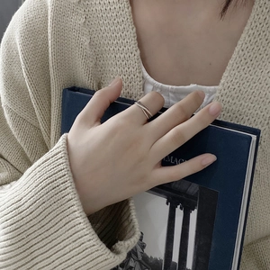 Minimalist silver woven ring on finger with soft knitwear and blue book background