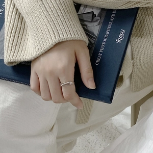 Silver woven knot ring styled on hand with a textured sweater and blue art book
