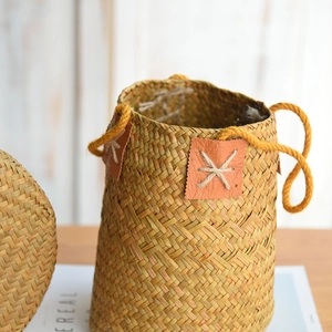 Natural seagrass woven flower basket with yellow rope handles on a wooden table