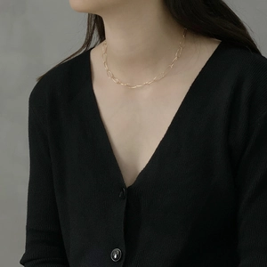 Minimalist golden long oval link chain choker necklace worn on a black V-neck cardigan