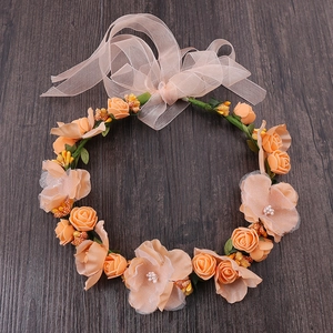 Top view of orange rose floral headband with champagne ribbon bow on dark wood