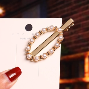 Detail shot of a gold-toned pearl duckbill hair clip with white oval pearls on card