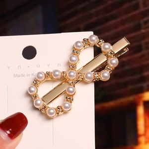 Close-up of golden infinity hair clip with white pearls and elegant duckbill design