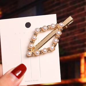 Detailed view of a gold geometric pearl hair clip with diamond accents on a brand card