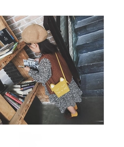 Girl wearing a yellow cat-shaped crossbody bag while reading in a retro library setting
