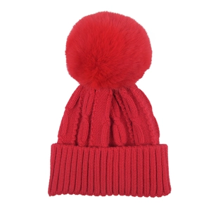 Close-up of red knitted cable pattern and large faux fur pompom on kids winter hat