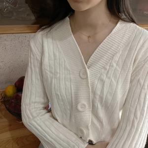 Close-up of a minimalist gold cross necklace on a white ribbed knit cardigan