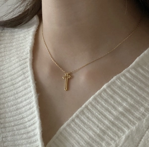 Close-up of a minimalist golden cross necklace worn over a white knitted sweater