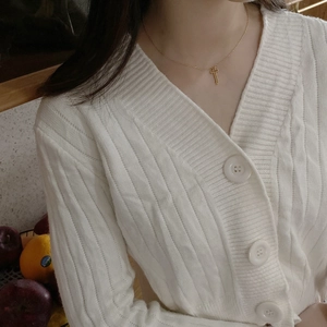 Close-up of a gold cross necklace worn with a white V-neck knitted cardigan