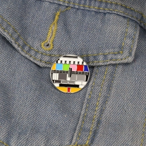 Retro TV color bars enamel pin displayed on a blue denim jacket pocket detail