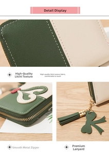 Detail of green and beige leather wallet featuring gold zipper and clover tassel charm