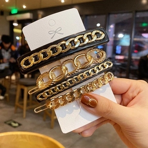 Detailed view of four golden chain hair clips with black acrylic accents on card