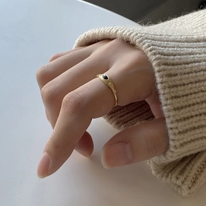 Close-up of gold 925 sterling silver ring with black evil eye on model in cozy knitwear
