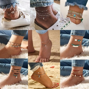 Detail von Boho-Fußkettchen mit Muscheln, Türkisperlen und Goldanhängern am Sandstrand