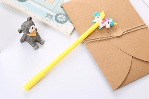 Close-up of a yellow cartoon unicorn gel pen with a colorful silicone topper on a desk