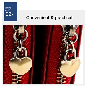 Detail of red leather wallet featuring dual heart-shaped brass zippers and textured finish