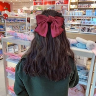Large red satin bow hair clip worn on a woman's hair back view detail for Christmas