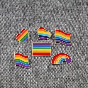 Set of 6 rainbow enamel pins on grey fabric showing heart and flag origami shapes