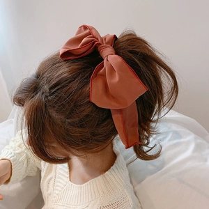 Brick red bow hair tie with red trim shown as a large fabric scrunchie ponytail accessory