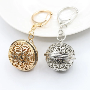 Golden and silver alloy hollow ball keychains on a white ceramic plate backdrop