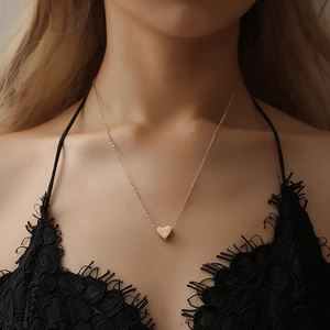 Minimalistische goldene Herz-Halskette an einem Modell mit schwarzem Spitzentop getragen