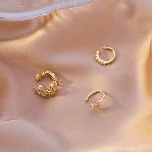 Three gold zircon ear cuffs with star pendants on champagne satin background