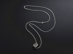 Macro detail of silver dice pendant and fine chain necklace on a dark textured background