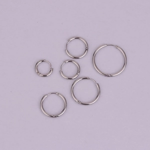 Flat lay of six stainless steel hoop earrings in three sizes on purple background