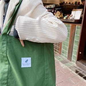 Close-up of green canvas tote bag with white patch detail on a casual street model
