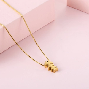 Elegant gold fishbone pendant necklace with thin snake chain on pink geometric background