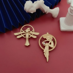 Close-up of vintage matte gold brooches with winged angel and pearl detail in art style
