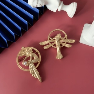 Detail of matte gold baroque angel brooches with brushed metal finish and pearl accents