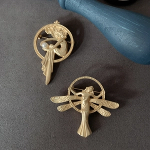 Detailed macro view of two vintage matte gold brooches featuring antique female silhouettes